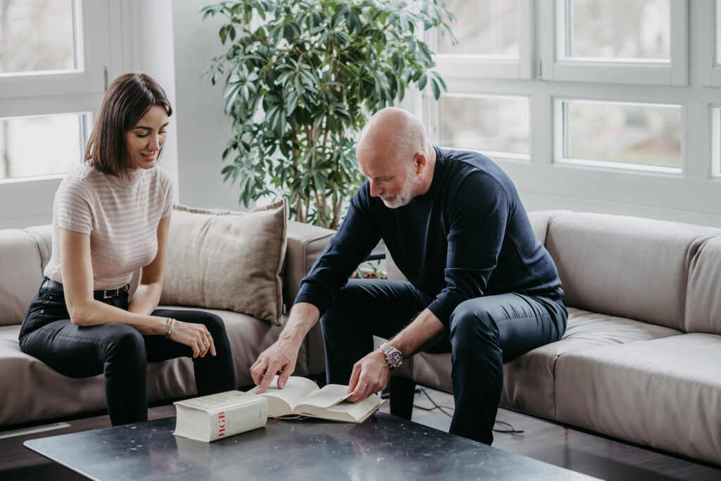 Das Bild zeigt Pervin Persenkli und Dr. Matthias Hallweger auf einem Sofa mit Blick auf ein Gesetzbuch.